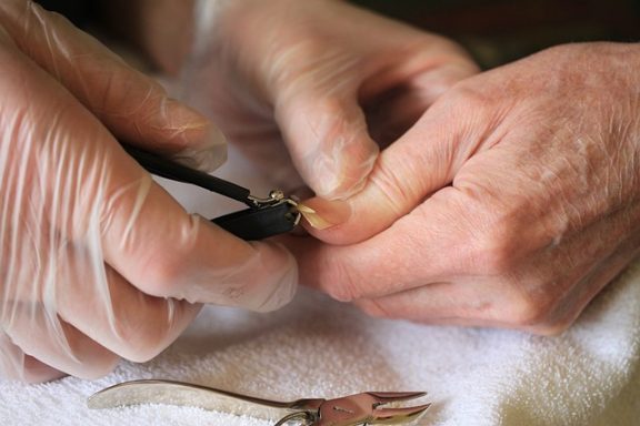 Manos con guantes utilizan un cortador para cuidar las uñas de otra persona.